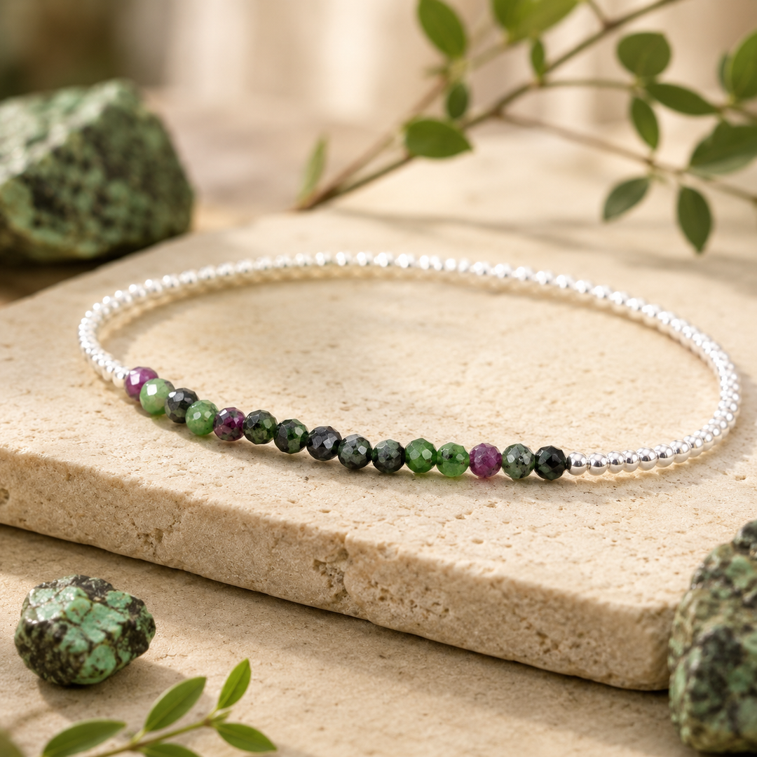 Beaded bracelet with green and purple stones on a natural stone surface with greenery.