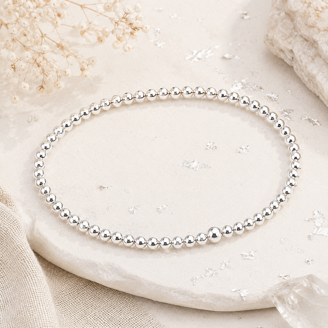 Silver beaded bracelet on a textured stone surface with delicate flowers