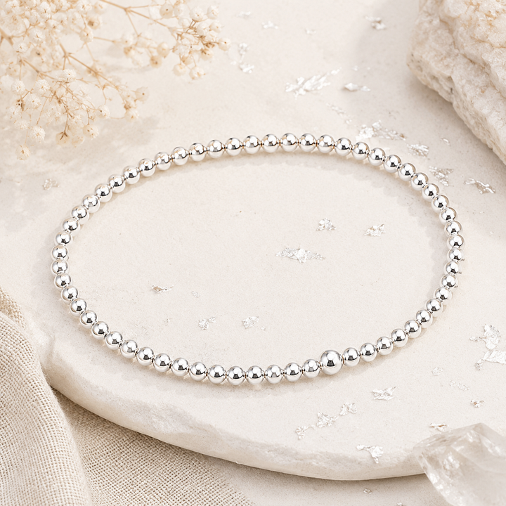 Silver beaded bracelet on a textured stone surface with delicate flowers