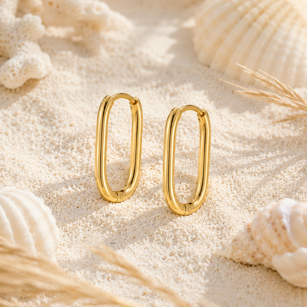 Waterproof gold oval hoops on a beach background.
