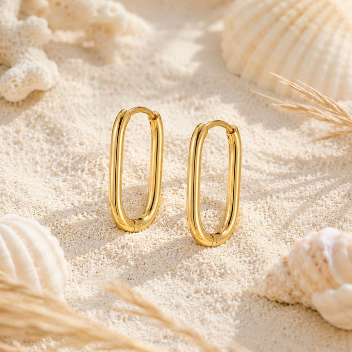 Waterproof gold oval hoops on a beach background.