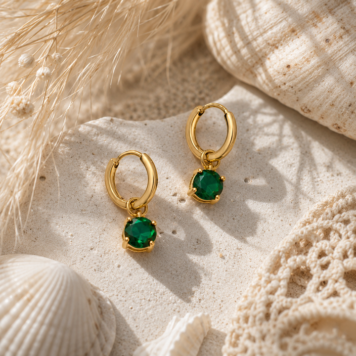 gold PVD waterproof huggies with emerald stone on a natural stone surface