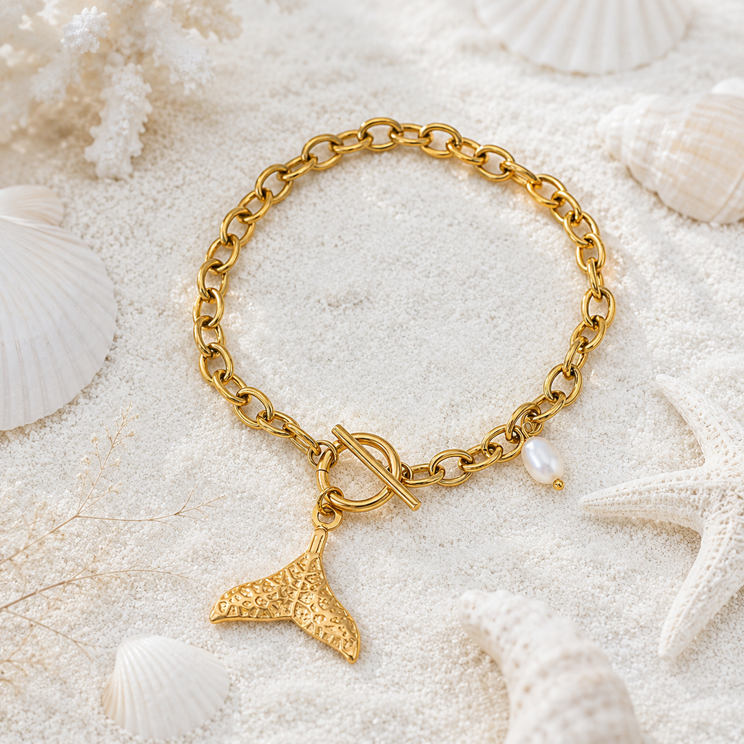 Waterproof gold whale tail bracelet with toggle closure in a beach setting.