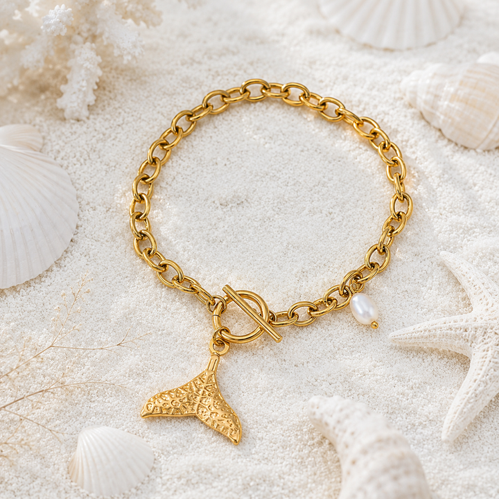 Waterproof gold whale tail bracelet with toggle closure in a beach setting.