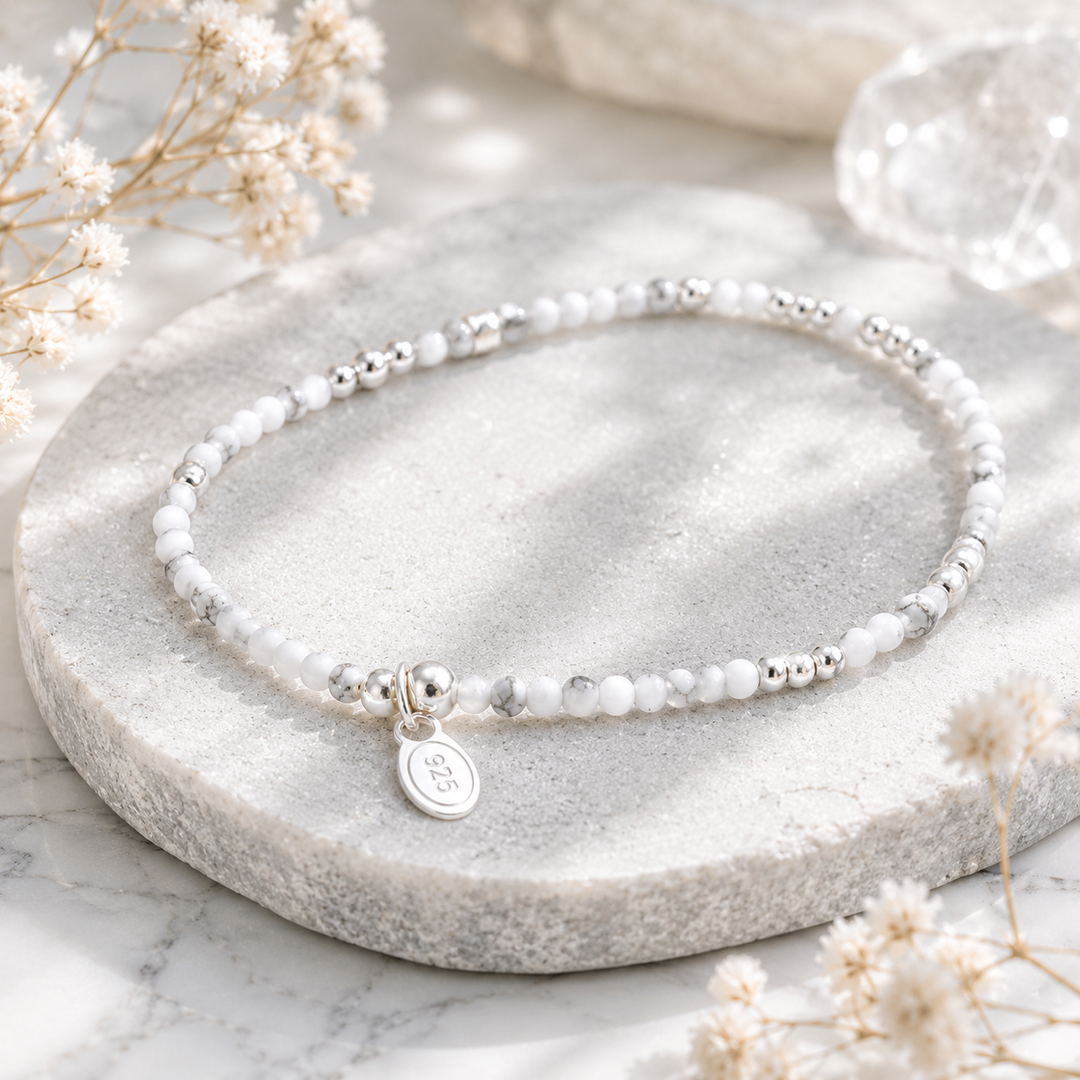 Natural white stone beaded bracelet with sterling silver charm on a marble surface with dried flowers.
