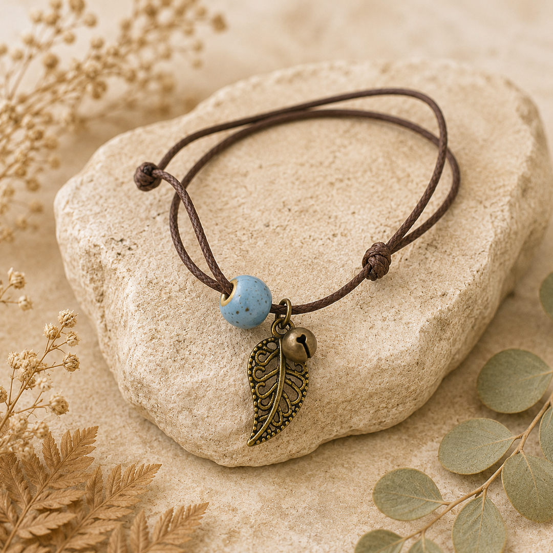 Anklet with leaf charm and blue bead on a stone surface with dried plants