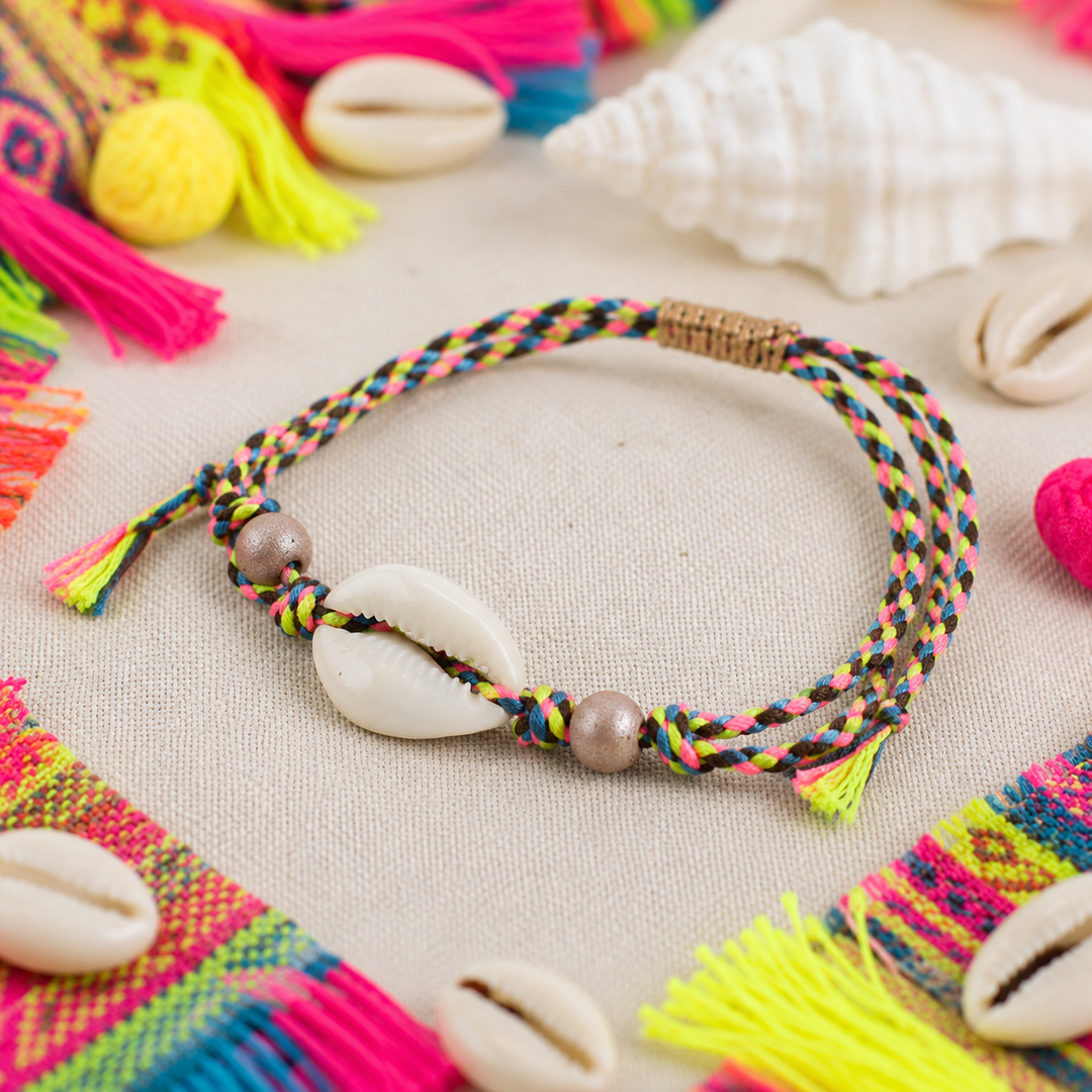 Colorful braided anklet with cowrie shells on a textured surface with colorful fabric and shells.