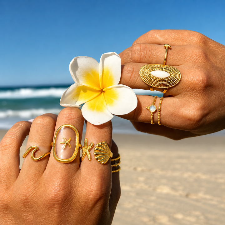 Hands with waterproof gold rings holding a white and yellow flower on a beach