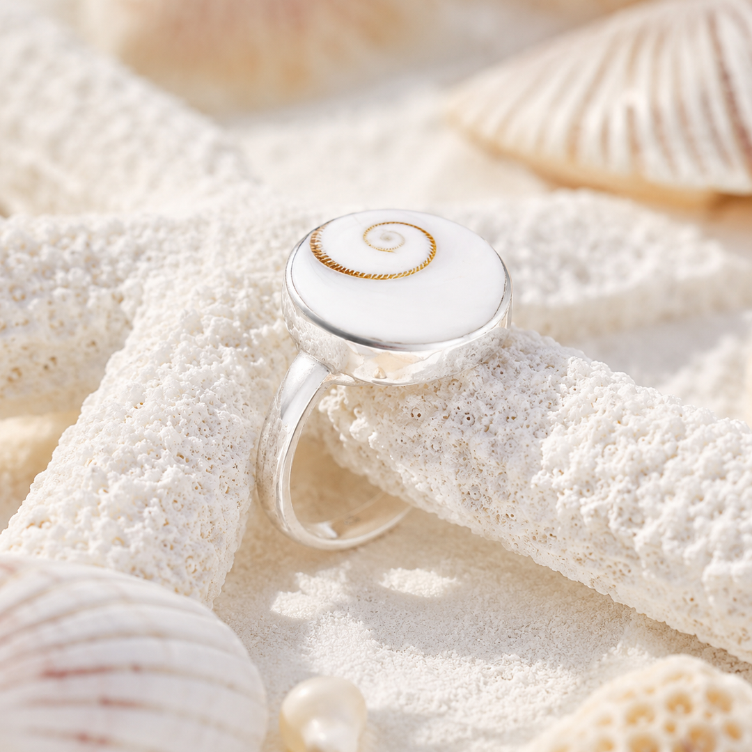 Silver ring with a shell design on a sandy background