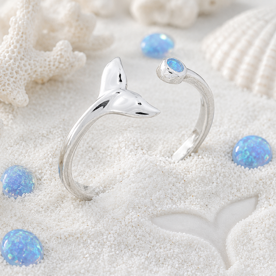 Silver whale tail shaped ring with opal stones on a sandy background