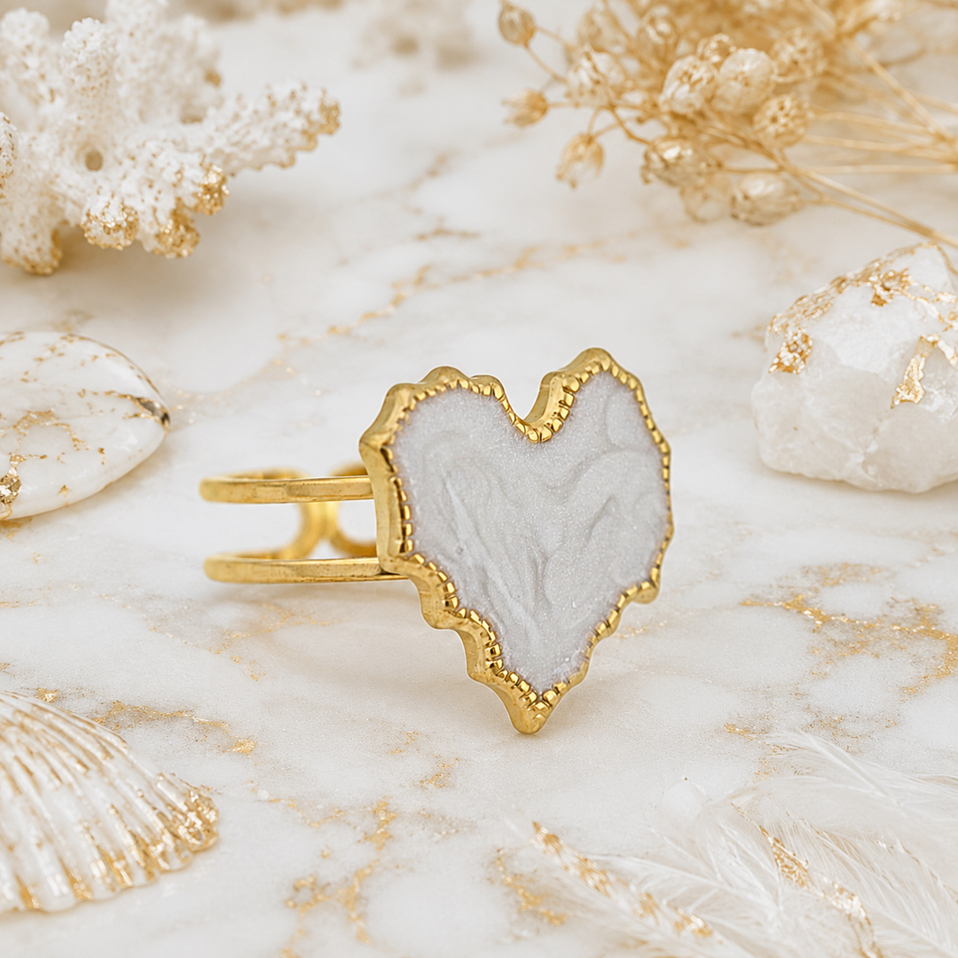 Heart-shaped ring with gold frame and white center on a shell background