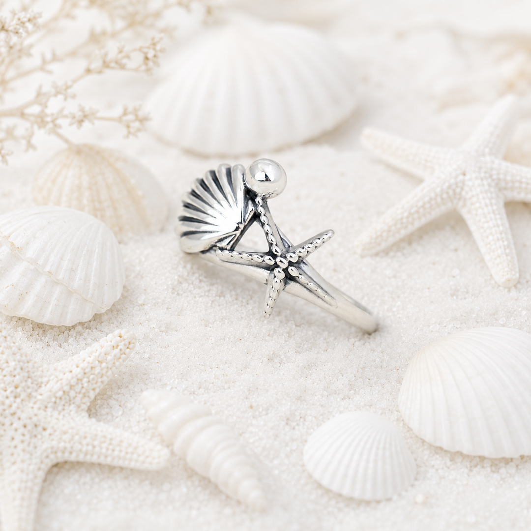 Silver ring with shell and starfish design on a sandy background