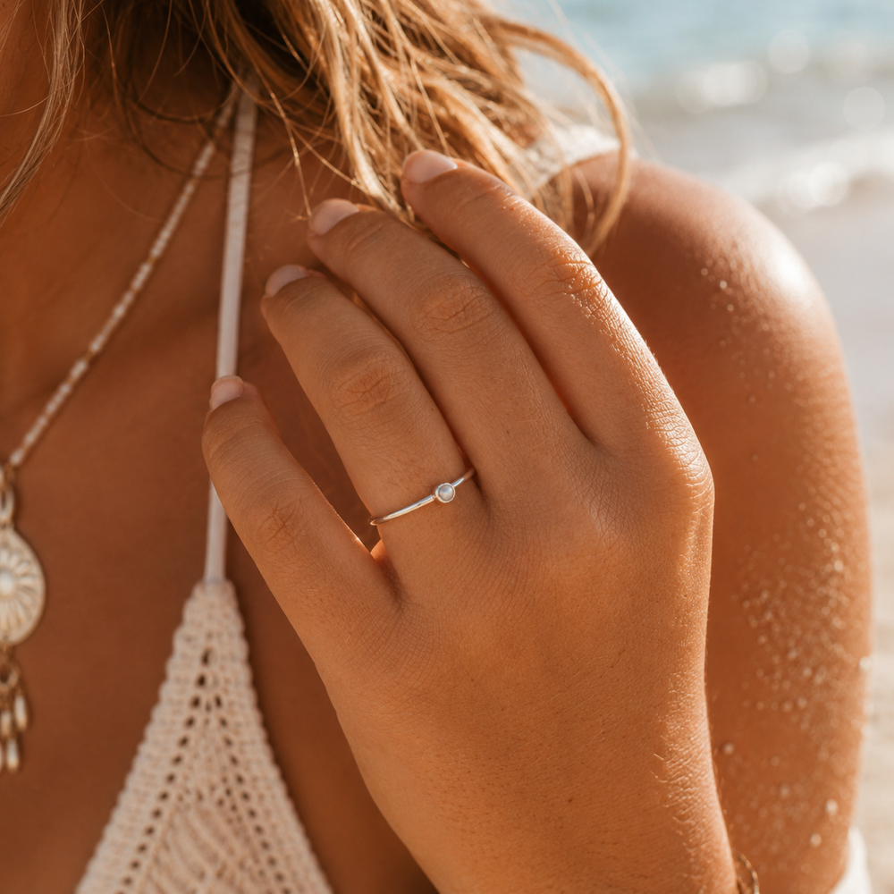 Close-up of a hand with a rdainty pearl ing on a beach