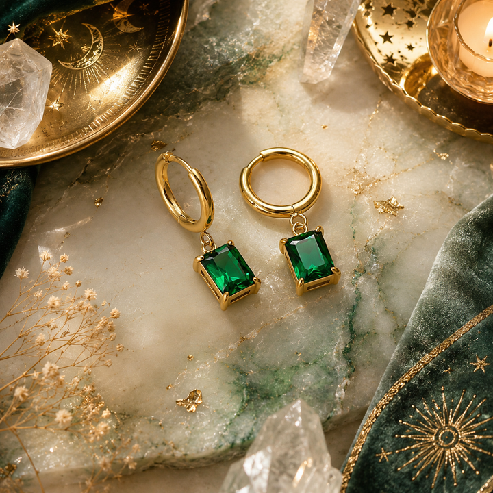 Waterproof Gold hoop earrings with emerald stone on a marble surface with crystals and candles.