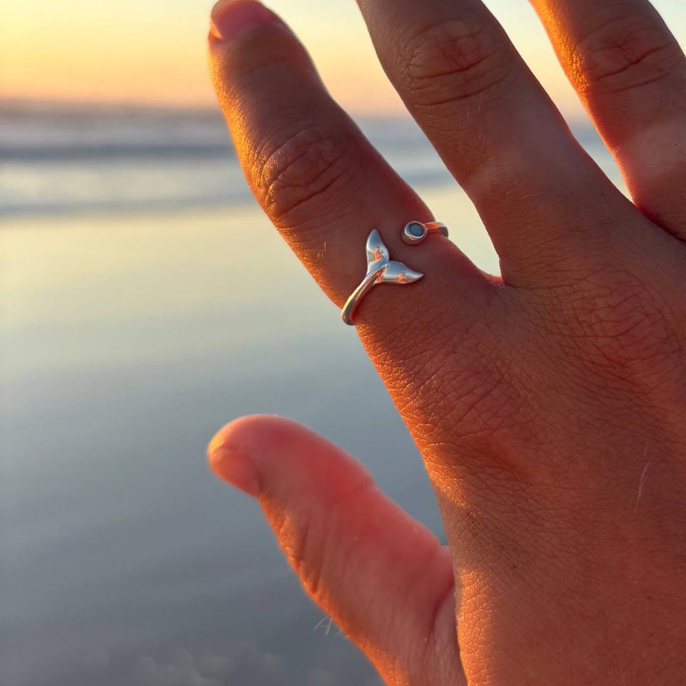 silver adjustable Azure Whale Tail Ring on hand in beach setting with sunset