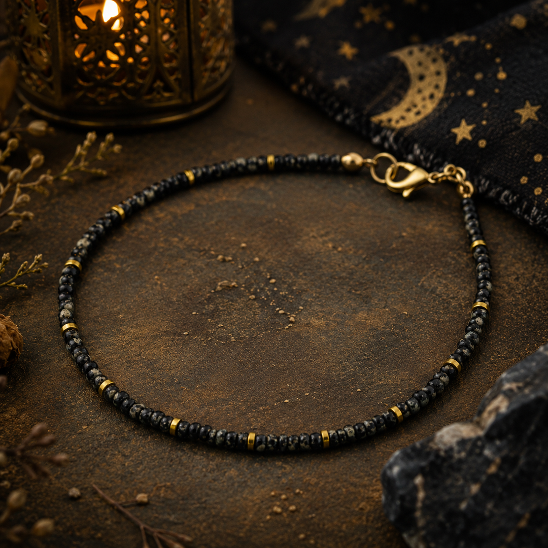 Black beaded anklet with gold accents on a dark surface with decorative elements.