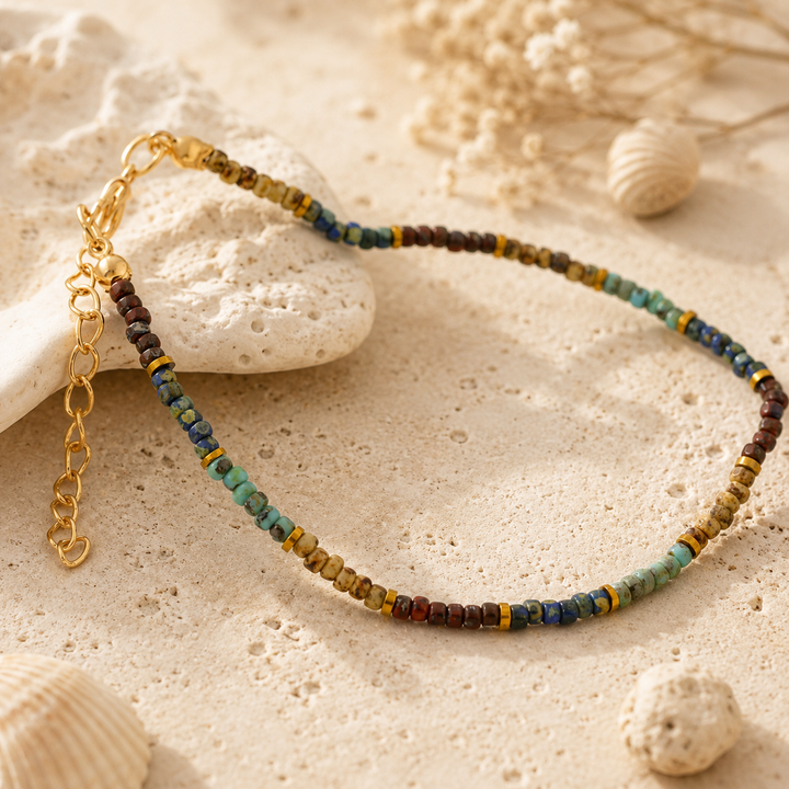 Multicolored banklet with gold chain on a sandy surface with shells.