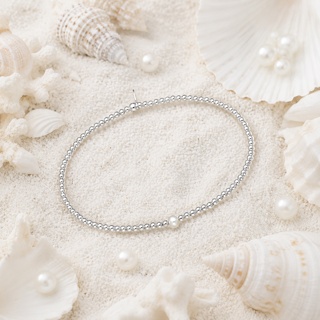 Silver beaded bracelet  with a single pearl on a sandy surface with seashells