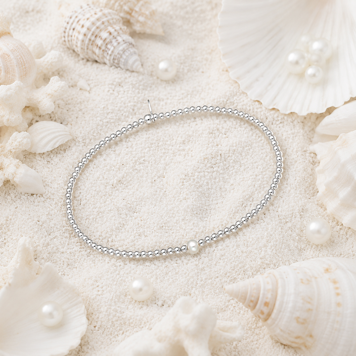 Silver beaded bracelet  with a single pearl on a sandy surface with seashells