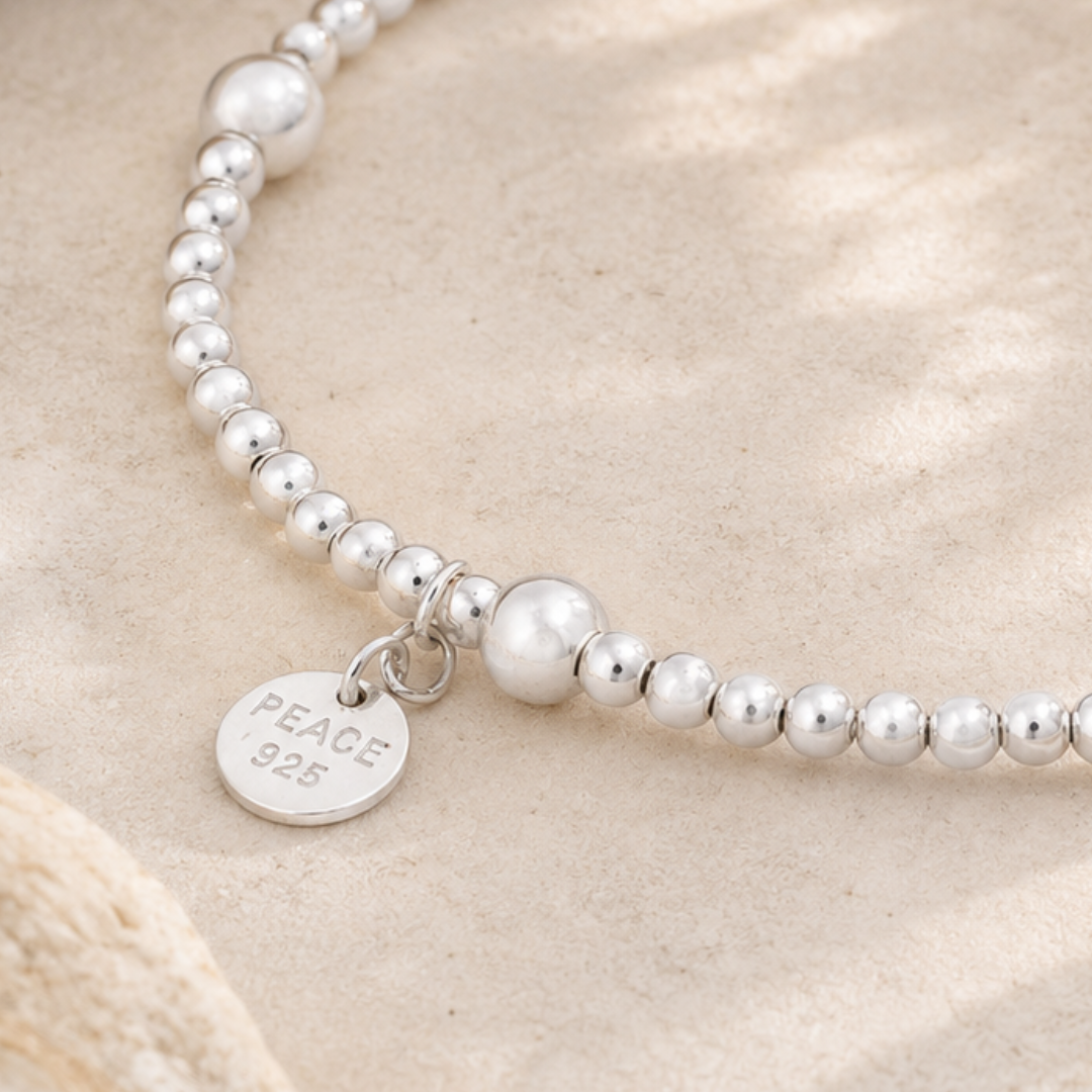 Silver beaded bracelet with a 'PEACE 925' tag on a beige background