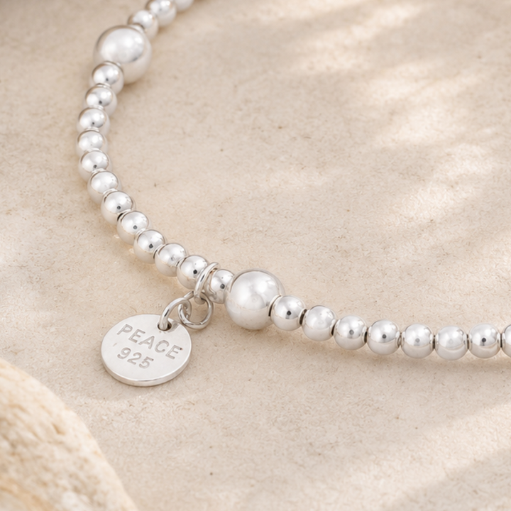 Silver beaded bracelet with a 'PEACE 925' tag on a beige background